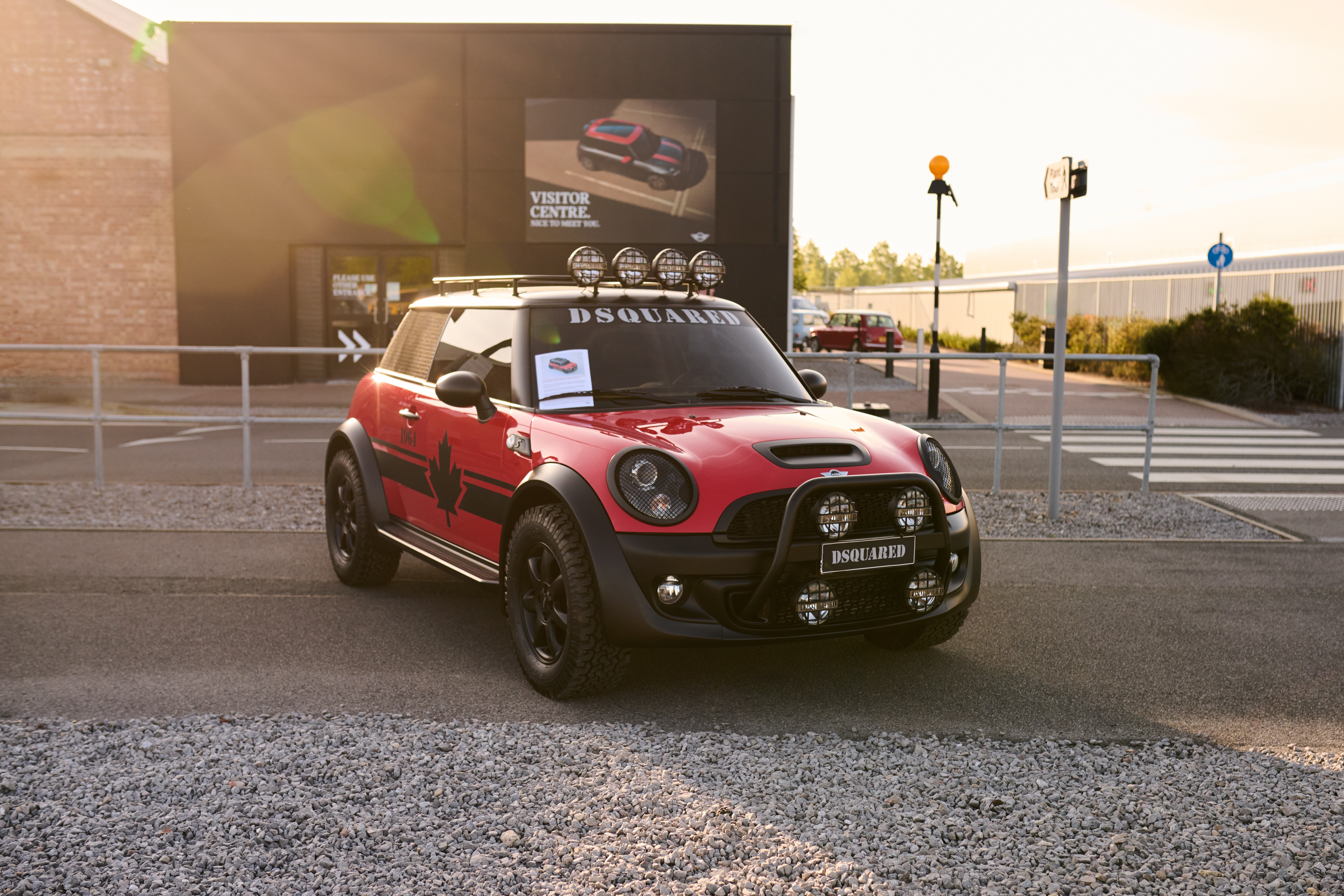 A silver Mini Cooper, adorned with Union Jack mirrors, speeds down a scenic road, followed closely by red and blue Minis among green blurred trees.